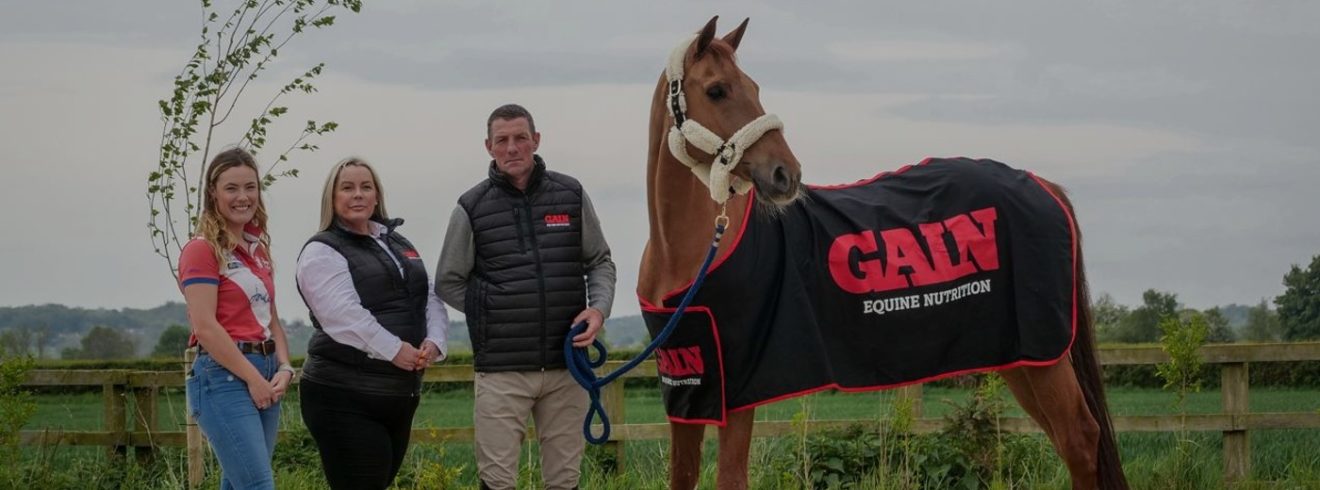 Two women and a man in GAIN jackets holding the leash to a horse covered in a GAIN equine nutrition horse cover.