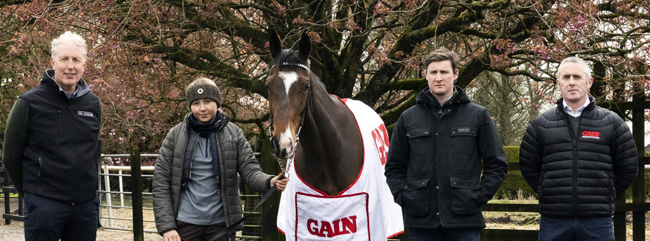 Four people standing with horse covered with a white and red GAIN horse cover.